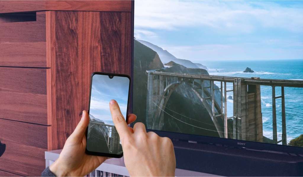 Two hands holding an iPhone that is casting an image of a coast to a Sony TV