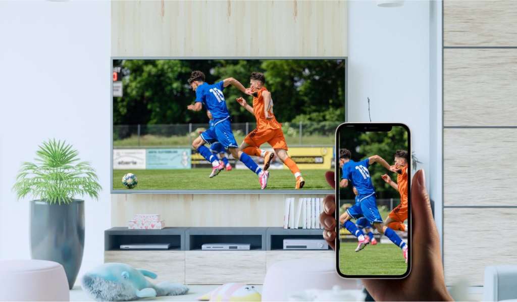 A hand holding an iPhone that is screen mirroring an image of a football match to a Philips TV