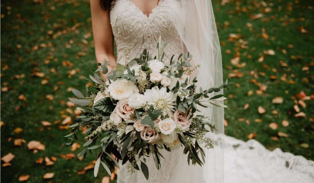 bride standing on grass with leaves, holding a bouquet of flowers