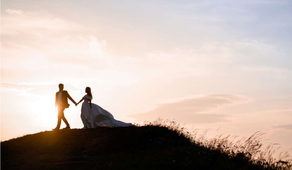 wedding couple walking on a hill holding hands during sunset